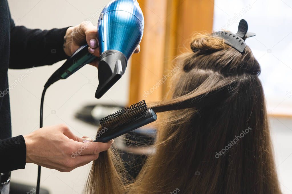 Master woman hairdresser dries the girls hair with a hairdryer and combs after washing in the beauty salon