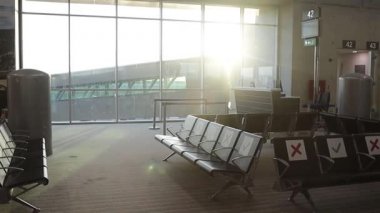 Covid-19 salgını sırasında havaalanı. Güneşin doğuşu, boş ayrılış ve bekleme alanını özel sosyal uzaklık işaretleri olan bir sandalyeden aydınlatır.