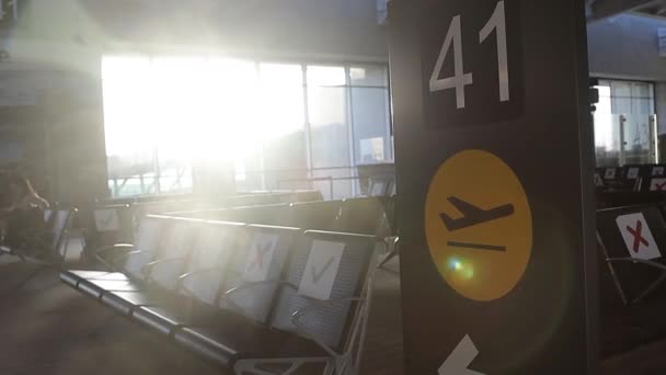 Flygplatsen under Covid-19-pandemin. Den uppgående solen på morgonen belyser den tomma avfärden och väntplatsen från en stol med speciella sociala avståndsskyltar — Stockvideo