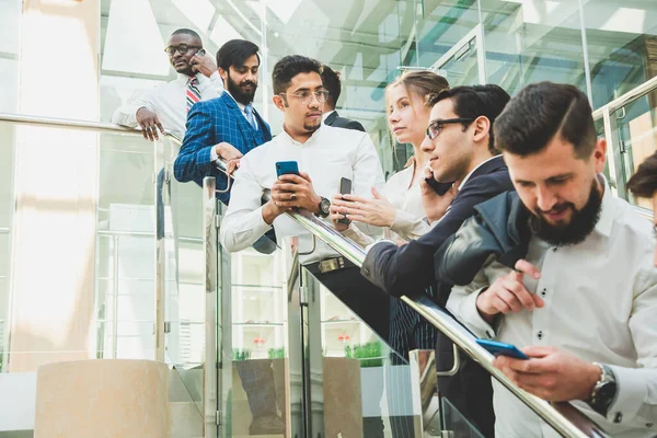 Jóvenes empresarios arego abajo de las escaleras y hablando en el fondo de las oficinas de vidrio. Corporativossteam y gerente en una reunión. — Foto de Stock