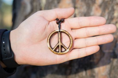 Ormanda avucunda tahta bir barış işareti kolyesi tutan bir adam, seçici bir odak noktası..