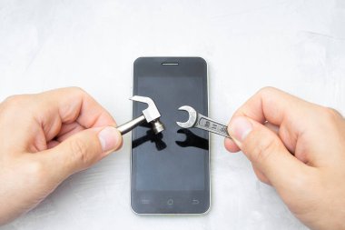 Küçük el aletlerini beton bir masada akıllı telefonun üzerinde tutan eller. Cep telefonu tamir kavramı.