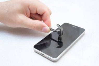 Küçük çelik bir çekiçle cep telefonunun ekranına çarpıyor..