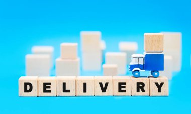 Minyatür kamyon, arkasında tahta küplerle DELIVERY okuyan harf bloklarının üzerinde duruyor. Yük teslimatı ve ofis taşıma kavramı.
