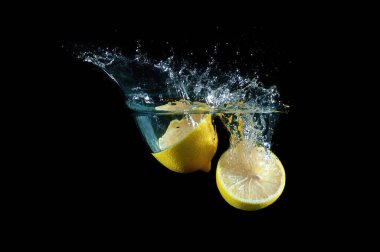 İki tane taze limon suyun derinliklerine doğru batıyor ve siyah bir zemin üzerinde sıçramalar oluyor.