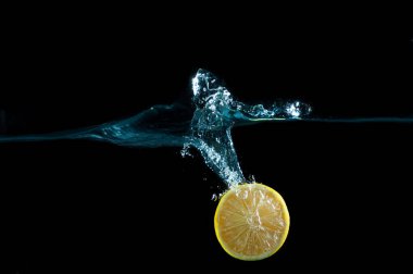 Suya düşen taze bir limonun yarısı siyah arka planda izole edilmiş.