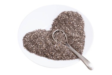 Beyaz bir tabakta küçük bir kaşıkla beyaz bir tabakta Chia tohumlarından yapılmış kalp sembolü.