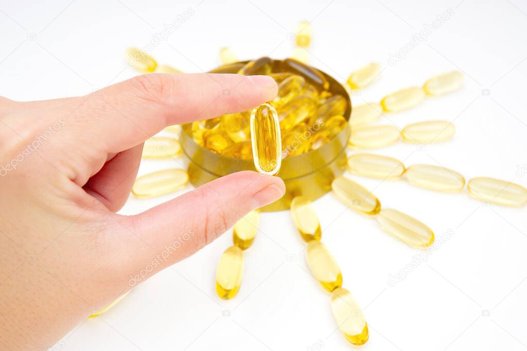 Fish oil capsule in hand. Omega-3 fatty acids softgels as a good source of Vitamin D.