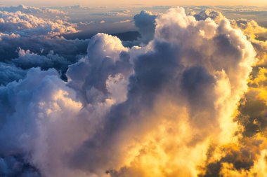 Scenic aerial view of the fluffy colorful clouds as seen through the airplane window at sunrise.