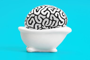 Steel copy of a human brain lying in a toy bath tub isolated on a blue background. Hot tub soaking for the mood lift.