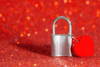 Small heart shaped pendant attached to a silver toned padlock against a glittering red background. Infinite true love concept.