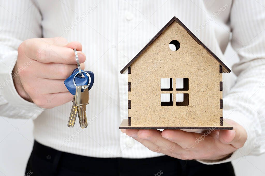 Man holding keys and a miniature wooden house model in hands. Get the keys day concept.