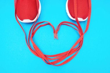 Kırmızı spor ayakkabılarının bağcıklarından yapılmış kalp sembolü mavi arka planda. Koşu konseptine aşık ol..