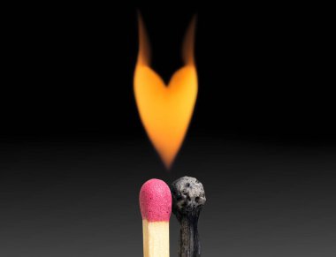 Bir çift kibrit çöpünden çıkan kalp şeklindeki alev koyu renk bir arka planda.