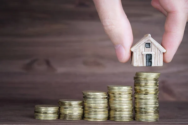 Bozuk paraların üstüne minyatür evler koymak ahşap bir arka plana karşı. Adım adım mortgage planı oluşturuluyor