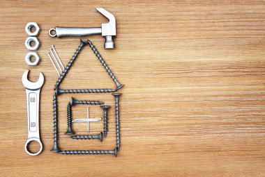 Tahta arka planda vida, çekiç, anahtar, fındık ve çivilerden yapılmış ev sembolü, boşluğu kopyala.