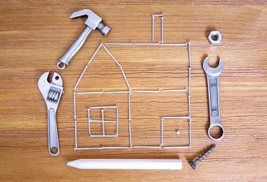 Ev şekli çivilerden, el aletlerinden ve ahşap arka plandaki bağlayıcılardan yapılmış. Ev onarım ipuçları ve hileleri kavramı.