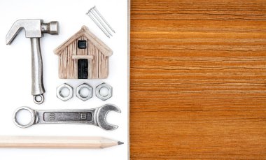 Minyatür oyuncak ev, küçük çekiç, ingiliz anahtarı, fındık, çivi, eskiz defteri ve tahta masadaki bir kalem. Ev geliştirme ve onarım planlama.