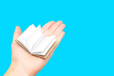 Mavi arka planda kadın elinin avucunda boş sayfaları olan minyatür açık bir kitap..