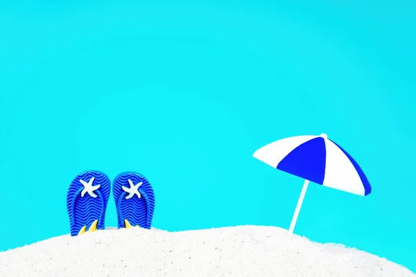 玩具的太阳伞和蓝色的翻筋斗从沙堆中伸出 映衬着蓝色的背景 模仿水 创意沙滩度假概念 — 图库照片