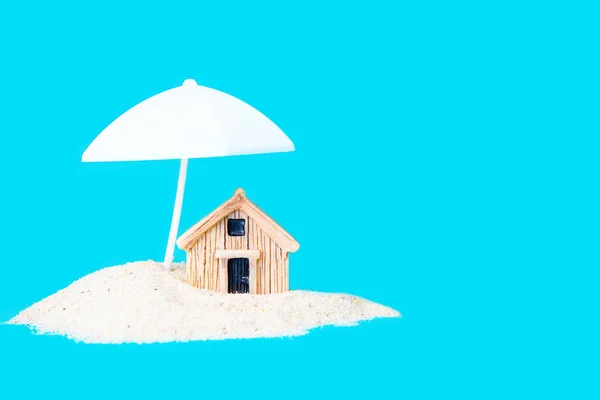 蓝色隔离的白色阳伞下的一堆沙子中的小玩具屋 创新的家庭保护概念 — 图库照片