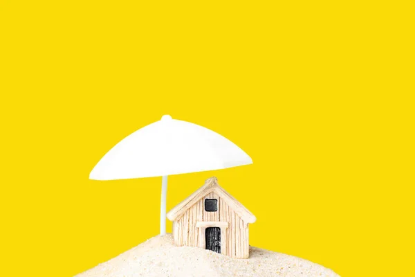 白色阳伞下的一堆沙子里 小玩具房子靠着黄色 创新财产保护概念 — 图库照片