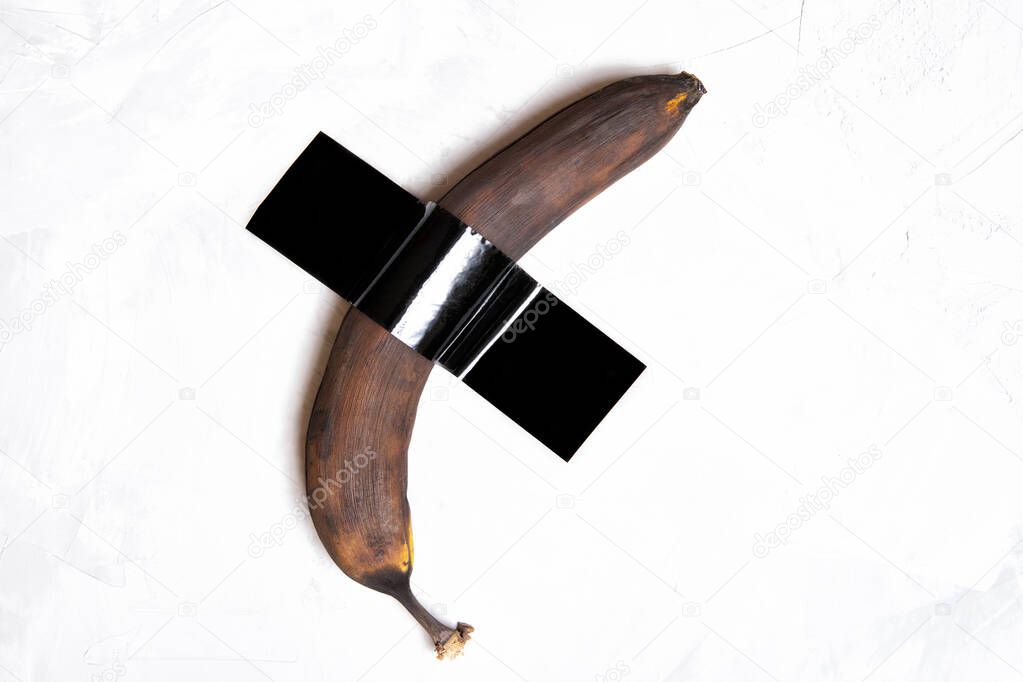 Brown banana attached to a concrete wall with a black duct-tape.