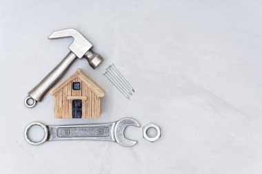 Minyatür oyuncak ev, küçük çekiç, ingiliz anahtarı, beton masa arka planında fındık ve çivi. Ev bakımı ve onarım konsepti.