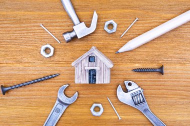 Minyatür bir oyuncak evin etrafında ahşap bir zeminde el aletleri ve bağlayıcılar var. Ev bakımı ve onarım konsepti.