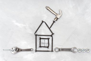Beton bir arka planda minyatür el aletleri ve bağlayıcılarla vida ve çivilerden yapılmış ev şekli. Ev onarımı kavramı.