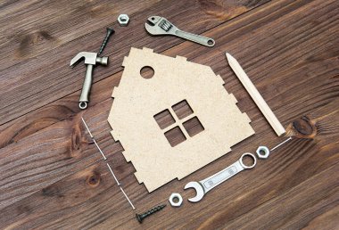 Temel el aletleri ve bağlayıcılar tahta bir arka planda minyatür düz bir ev şeklinde dizilmiş. Ev geliştirme ve onarım kavramı.