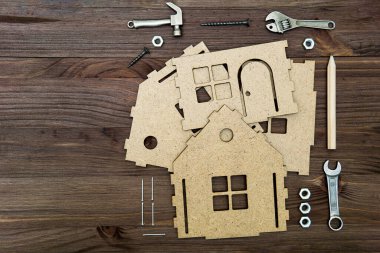 Minyatür el aletleri ve bağlayıcıları olan mukavva ev modelinin parçaları ahşap bir arka planda fotokopi alanı ile düzenlenmiş..