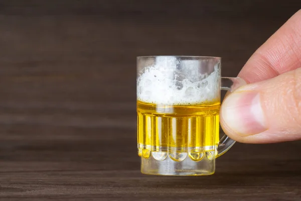 Erkek parmaklar minyatür bir bira bardağını ahşap bir masa arkasında tutuyor. Alkol ılımlı tüketim kavramı