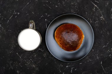 Siyah bir tabakta, siyah desenli arka planda bir bardak taze sütle ev yapımı poğaça. Düz konum, stüdyo çekimi, kopyalama alanı.