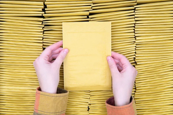 女用手拿着一个充填的信封在一堆堆叠在一起的黄色泡沫邮件上的头像 复制空间 产品检验和质量控制 — 图库照片
