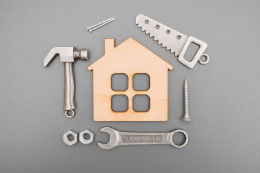 Essential hand tools and fasteners arranged around a miniature flat house model on gray background