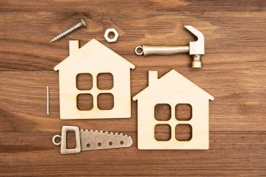 Two wooden flat house models and small steel copies of essential work tools and fasteners arranged on a wooden background.