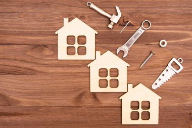 Üç ahşap düz ev modeli ve el aletleri ve bağlayıcıların küçük çelik kopyaları kopya alanı olan ahşap bir arka plana yerleştirilmiş..