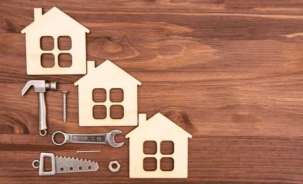 Temel iş aletlerinin minyatür kopyaları ve bağlayıcıları olan üç ahşap düz ev modeli fotokopi alanı ile ahşap bir arka plana yerleştirildi..