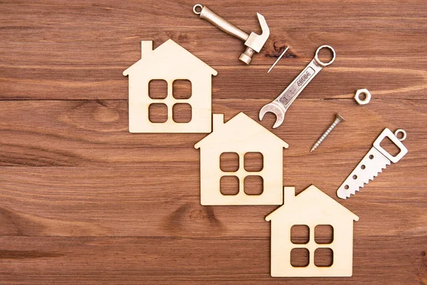 Üç ahşap düz ev modeli ve el aletleri ve bağlayıcıların küçük çelik kopyaları kopya alanı olan ahşap bir arka plana yerleştirilmiş..