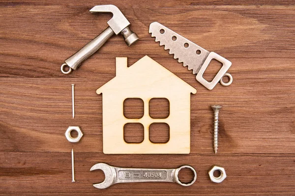 Temel iş aletlerinin minyatür kopyaları ve ahşap bir ev modelinin etrafına yerleştirilmiş bağlayıcılar. Ev geliştirme düz-yatay.