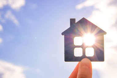 Mavi gökyüzü arka planında düz ahşap bir evi tutan el..