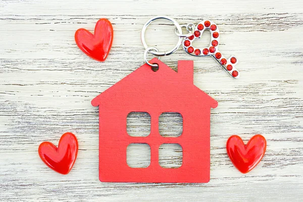 Kırmızı elmaslarla süslenmiş küçük kalp şeklinde anahtar, düz ev şekilli anahtarlık ve tahta arka planda küçük kırmızı kalpler. Güzel ev romantik konsept.