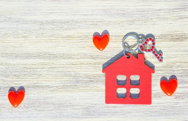 Takma elmaslarla süslenmiş anahtar, kırmızı ev şekilli anahtarlık ve tahta arka planda küçük kalpler. Romantik taşınma konsepti.