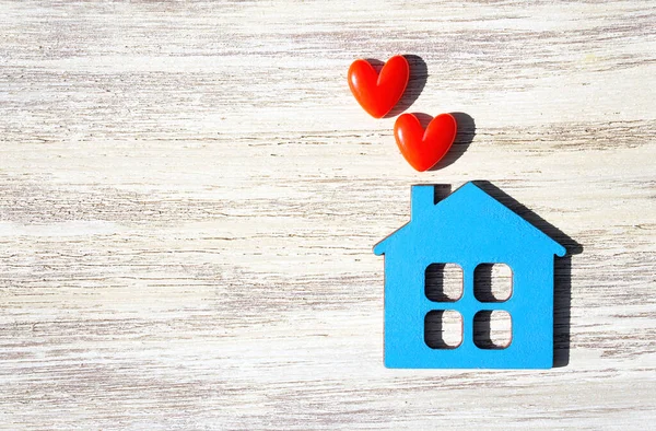 Düz mavi ev şekli, iki küçük kırmızı kalp ve kopya alanı olan ahşap bir masa..