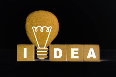 Tahta bloklardan yapılmış IDEA harfleri ve siyah arkaplanda düz bir ampul şekli.