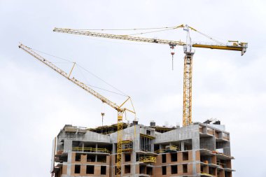 Gökyüzü arka planında iki kule vinci olan ev inşaatı.