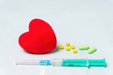 Büyük kırmızı kalp şekli, şırınga ve gri arka planda fotokopi alanı olan haplar. Kalp tedavisi kavramı.