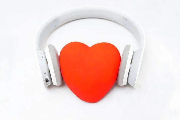 ワイヤレスヘッドフォンは ニュートラルな背景に大きな赤いハートを置きます 音楽を聴くことで心を癒す — ストック写真
