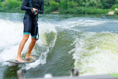 Nehirde bir teknenin arkasında wakeboard süren bir erkek.